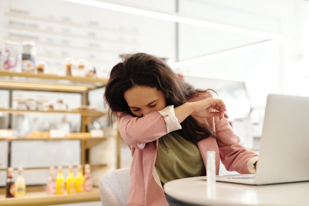 woman coughing into arm office worker returning to work after illness